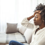 Young black woman sitting on her couch with a headache from a car accident