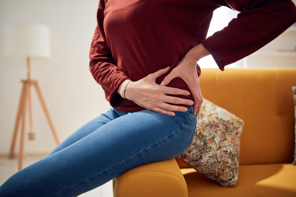 Woman sitting on couch with her hands on her hip because of hip pain