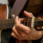 Close-up of the hands of a musician playing the guitar. The fingers of the musician are pressing the strings on the guitar.