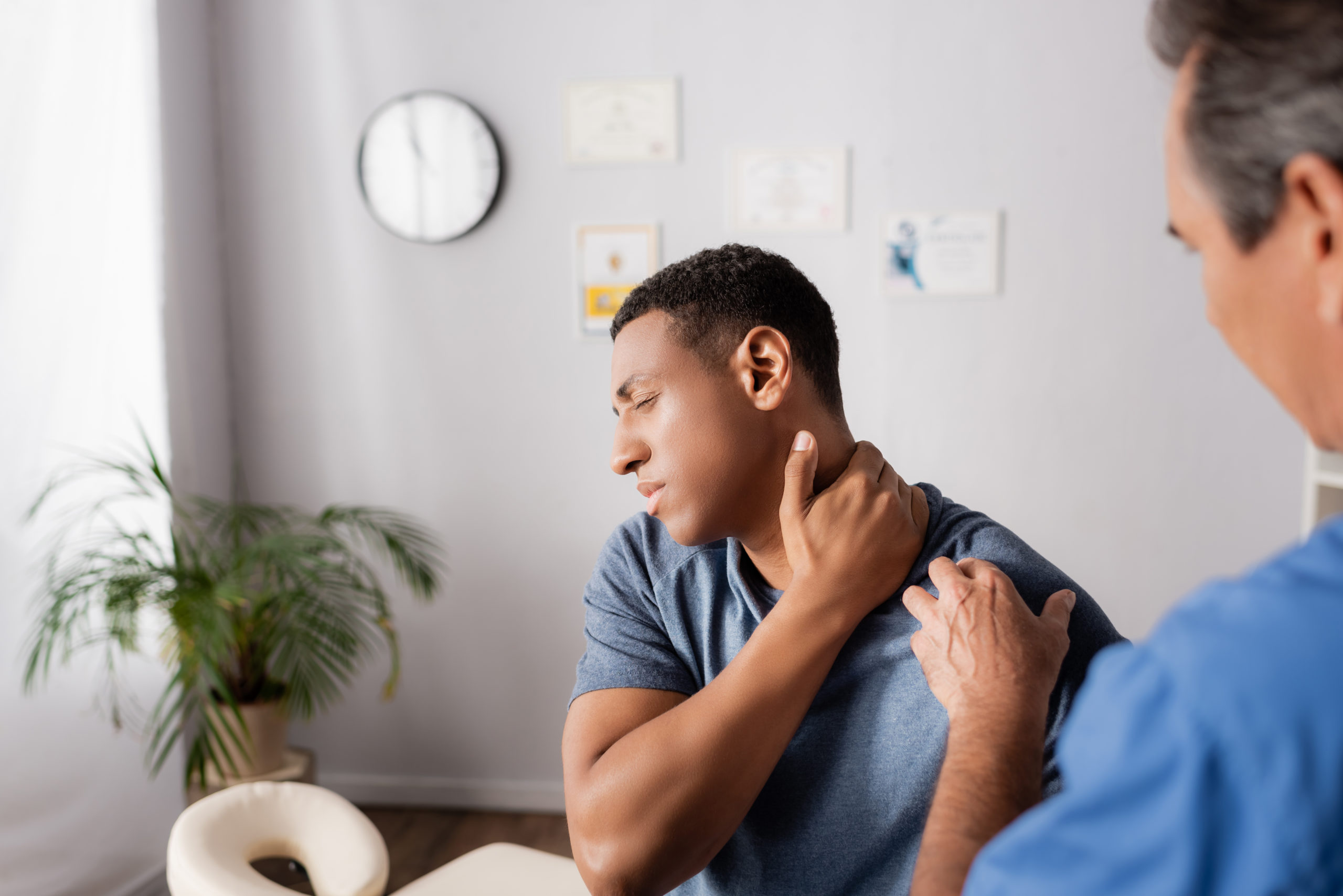 Man in doctor's office holding his neck as if injured