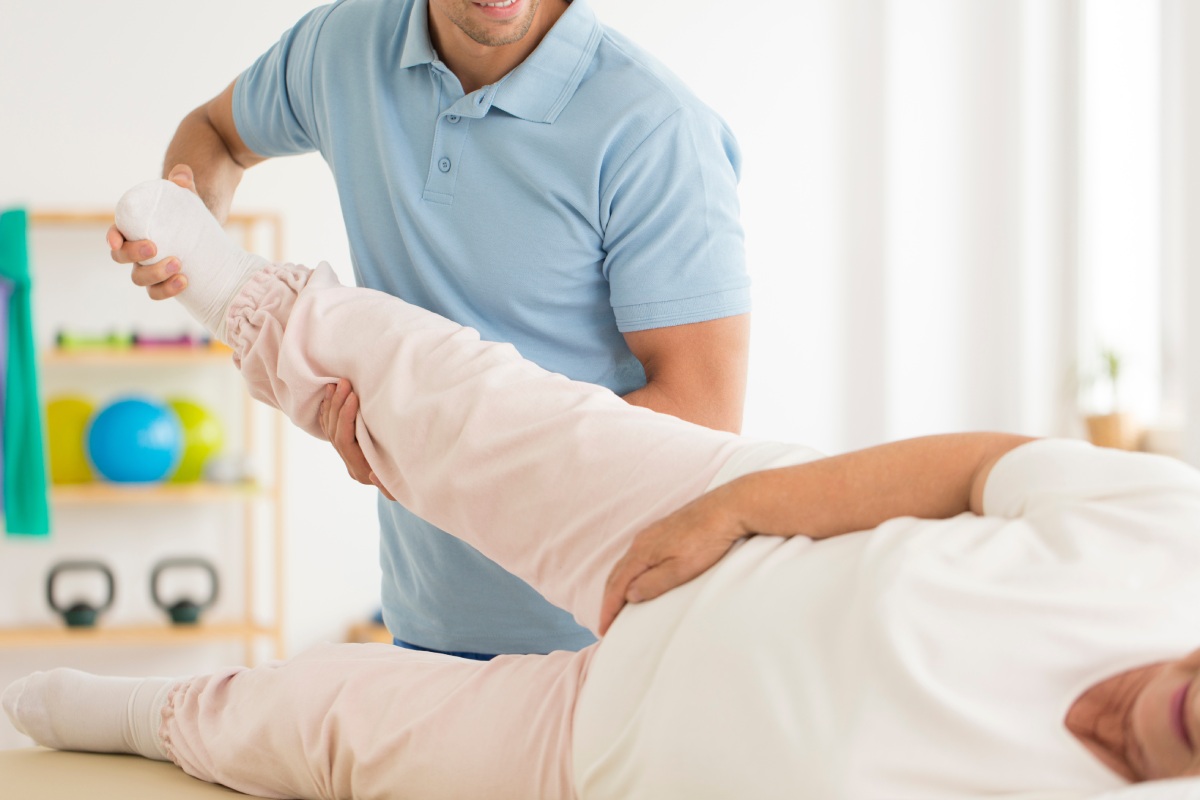 A person safely stretching their hip after a replacement with help of a doctor