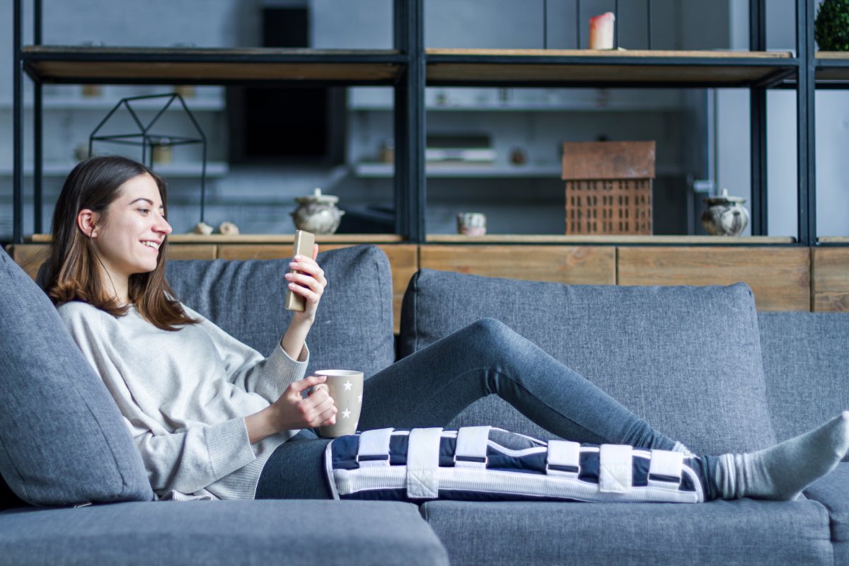 A woman resting on the couch with knee brace on recovering from a car accident