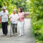 An older woman with a cane is walking with her husband and daughter after recovering from hip surgery.