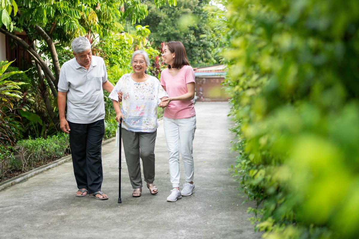 An older woman with a cane is walking with her husband and daughter after recovering from hip surgery.