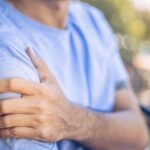 A man in a blue shirt holding his right shoulder in pain.