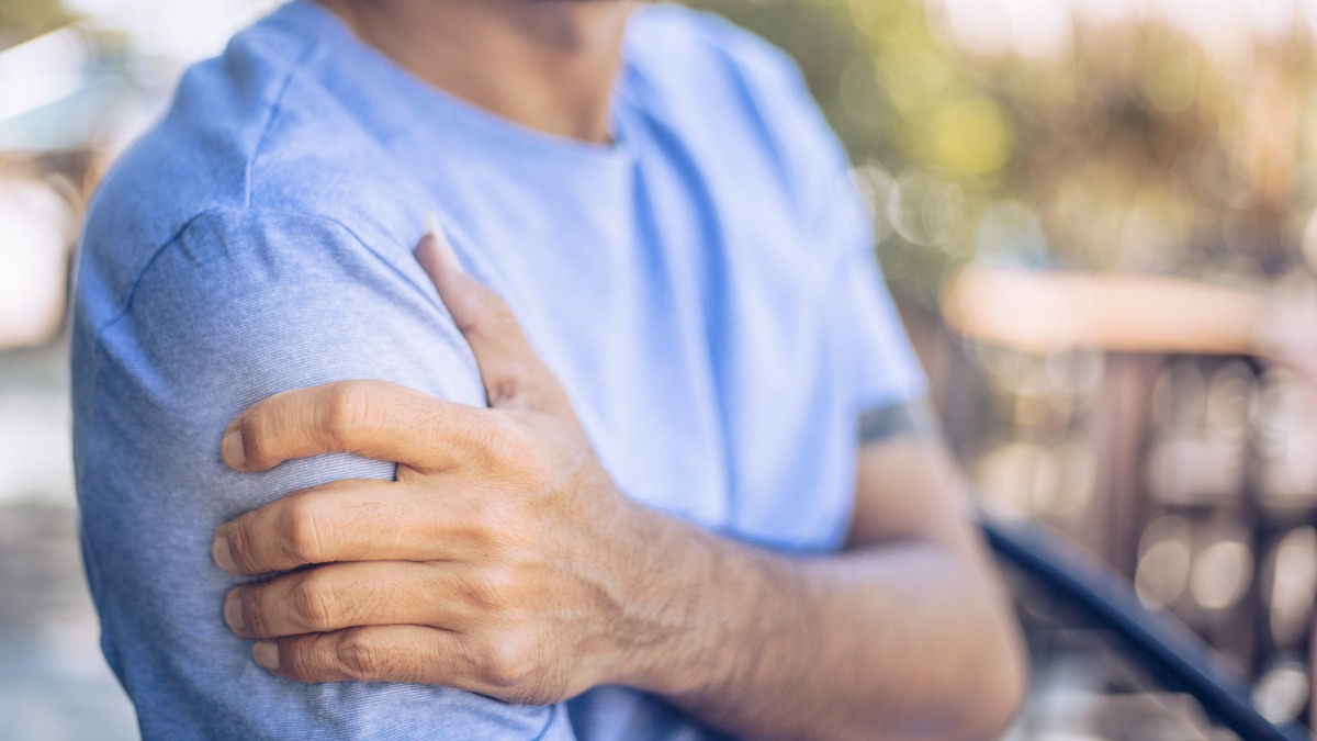 A man in a blue shirt holding his right shoulder in pain.