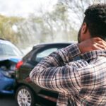 Young male driver with whiplash injury standing by damaged car after car accident.