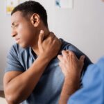 Man holding his neck in pain while being examined by a healthcare professional, illustrating common neck injury symptoms.