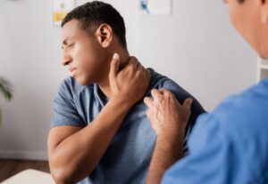 Man holding his neck in pain while being examined by a healthcare professional, illustrating common neck injury symptoms.