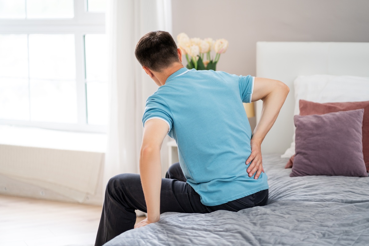 chronic-back-pain Man sitting on bed holding his lower back in pain, representing chronic back pain that may be treated with endoscopic rhizotomy.