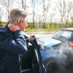 Older man holding his neck in pain after a rear-end car accident, illustrating a common whiplash injury caused by vehicle collisions.
