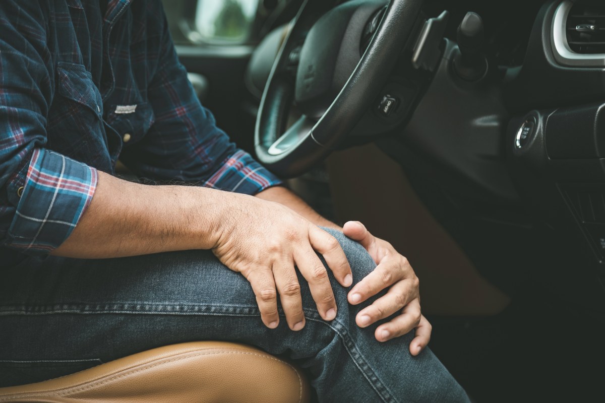 A man sitting in his car grasps his knee in pain after a knee injury from a car accident.