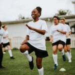 A group of women soccer players doing warm-up exercises with a coach on a grassy field. The focus is on injury prevention and strengthening—key elements of ACL injury prevention and surgery recovery and rehabilitation.
