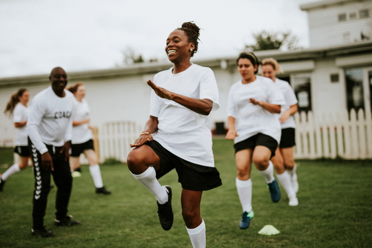 A group of women soccer players doing warm-up exercises with a coach on a grassy field. The focus is on injury prevention and strengthening—key elements of ACL injury prevention and surgery recovery and rehabilitation.