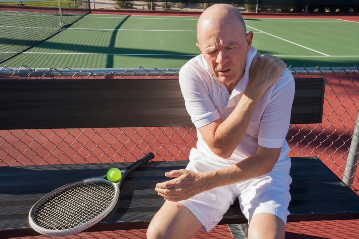 Man sitting on a tennis court holding his shoulder, a common injury that may require rotator cuff surgery.