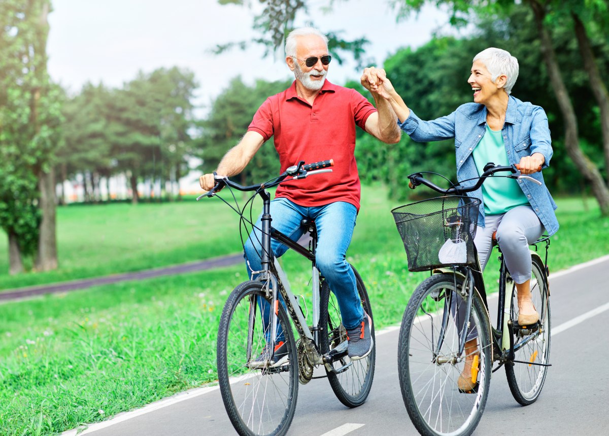 Active older couple riding bicycles and smiling in a park, symbolizing improved mobility after hip surgery recovery time.