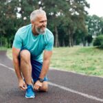 Older man bending down to tie his shoes. He is going for a run after recovering from robotic knee replacement.