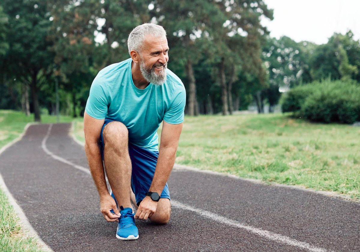 Older man bending down to tie his shoes. He is going for a run after recovering from robotic knee replacement.