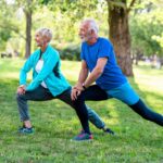 An older couple performing stretches on grass in a sunny park. This active, post-rehab scene reflects what's possible after knee surgery recovery time with consistent physical therapy.