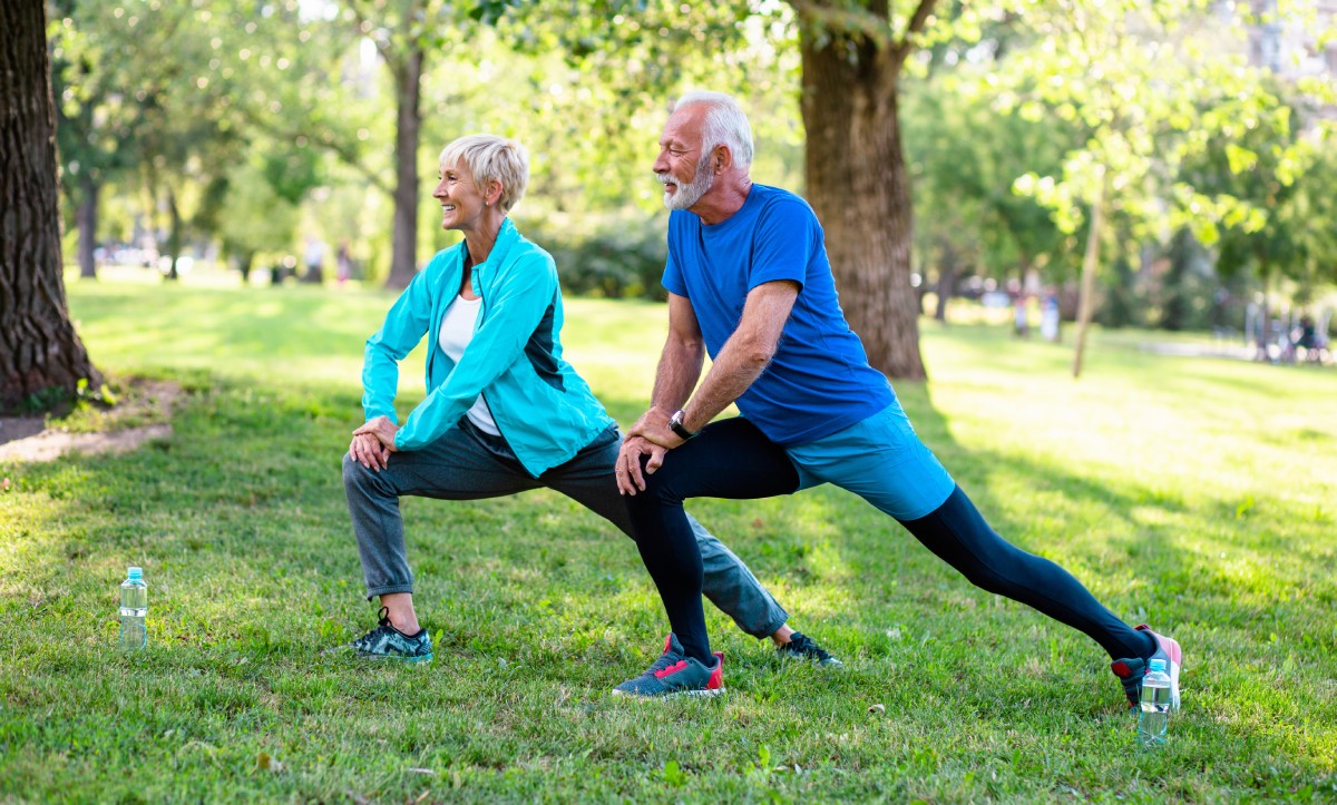 An older couple performing stretches on grass in a sunny park. This active, post-rehab scene reflects what's possible after knee surgery recovery time with consistent physical therapy.