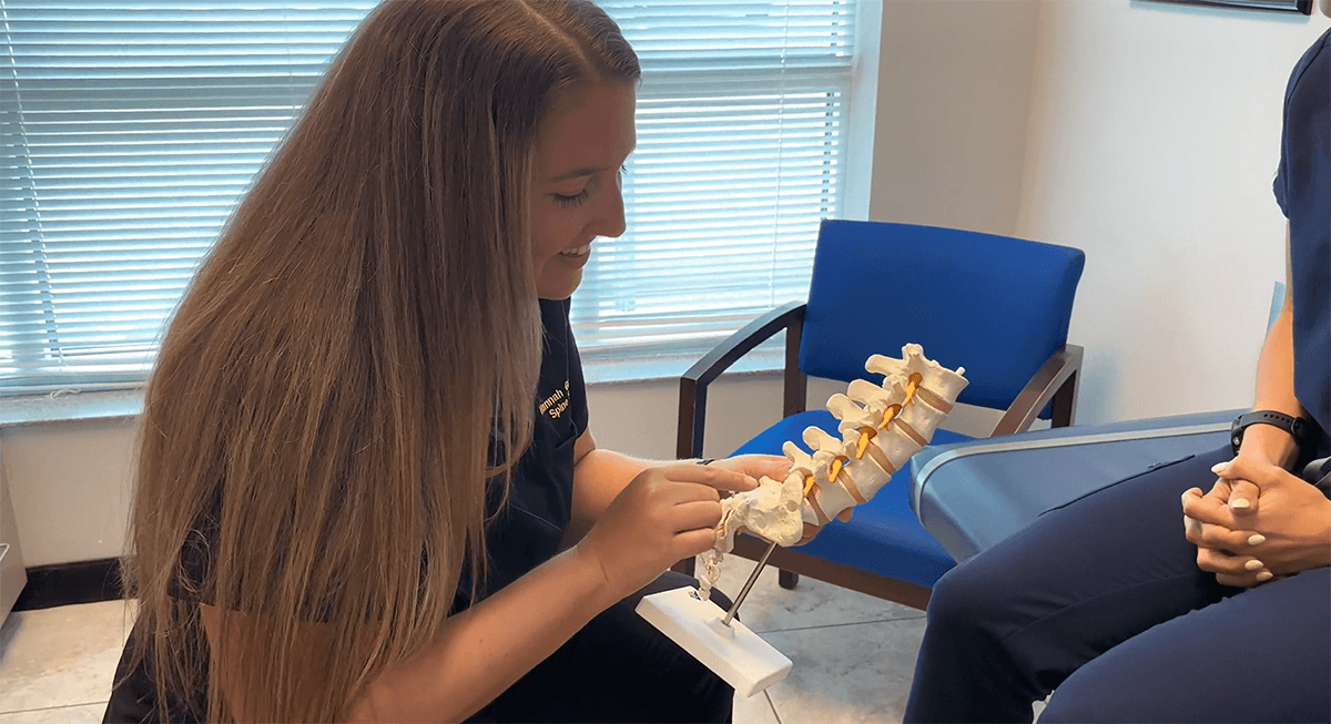 Dr. Groff holding a model of a spine and discussing treatment with a patient.