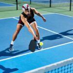 Man playing pickleball on a blue court reaches out to hit the ball with his paddle.