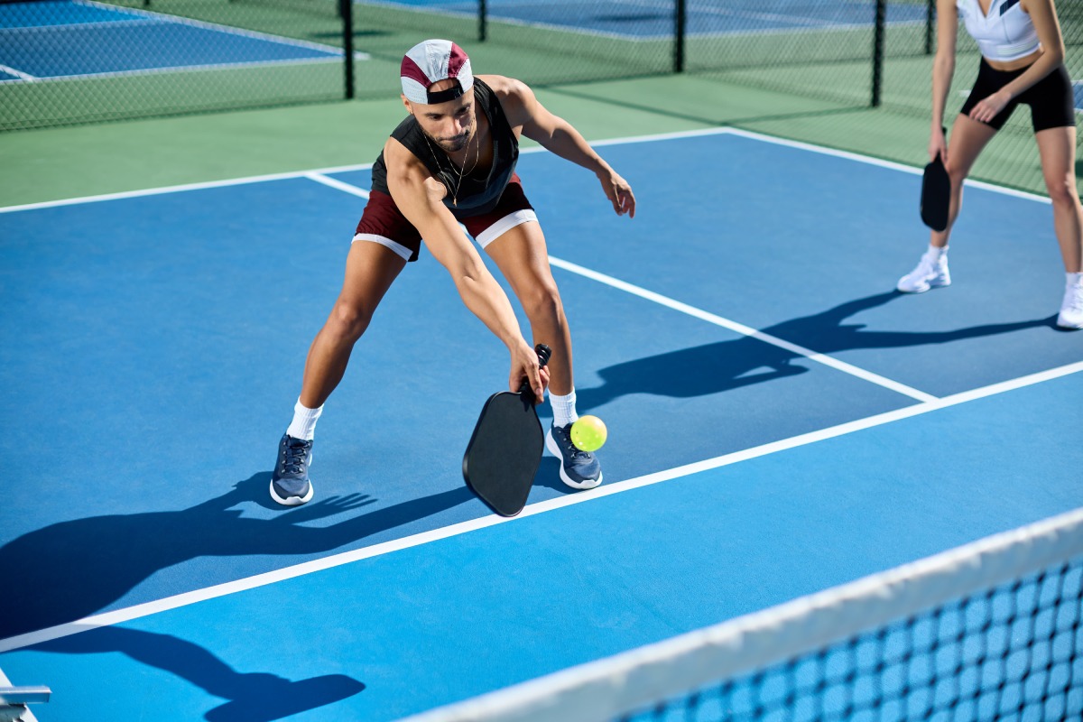 Man playing pickleball on a blue court reaches out to hit the ball with his paddle.